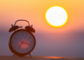 Zegar budzik z tłem wschodzącego słońca, reprezentujący korzyści wcześniejszego wstawania.