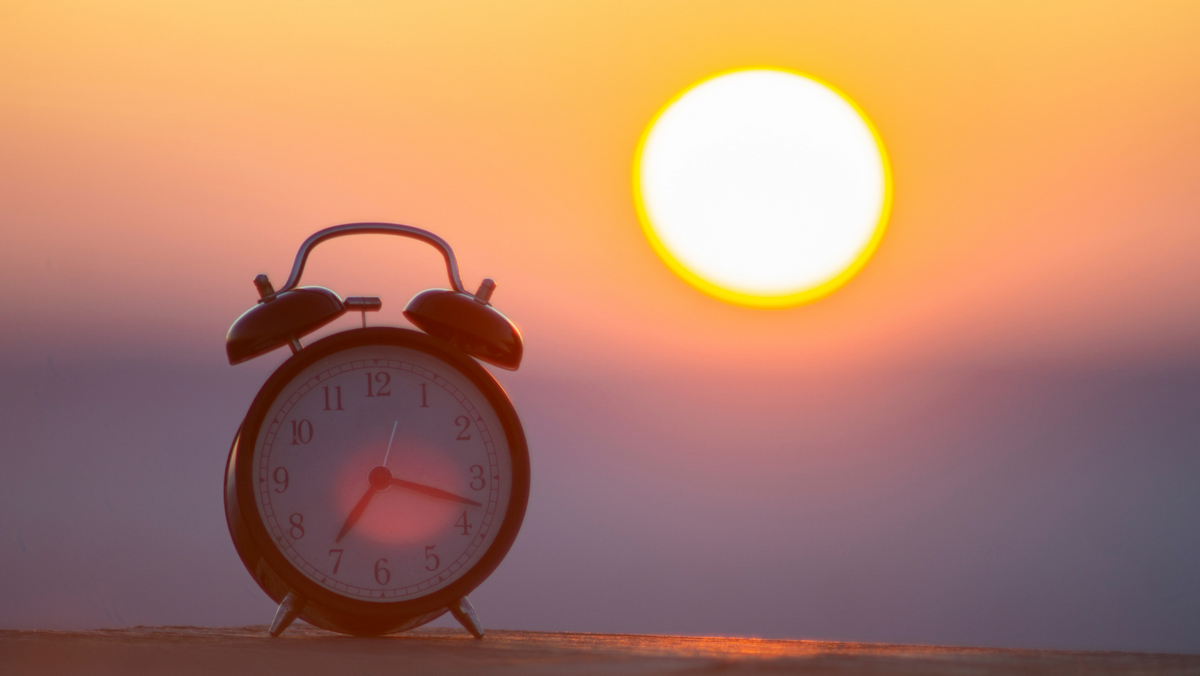 Zegar budzik z tłem wschodzącego słońca, reprezentujący korzyści wcześniejszego wstawania.